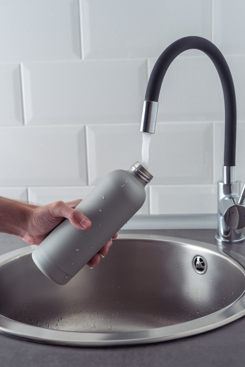 Hand hält Metall-Wasserflasche unter einen Wasserhahn über einem Spülbecken